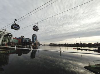 Overhead cable car over river in city against sky