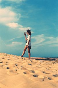 Side view of woman standing at desert against blue sky