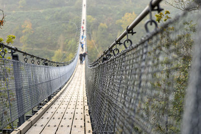Suspension wooden bridge with steel ropes over a dense forest in west germany, visible tourists