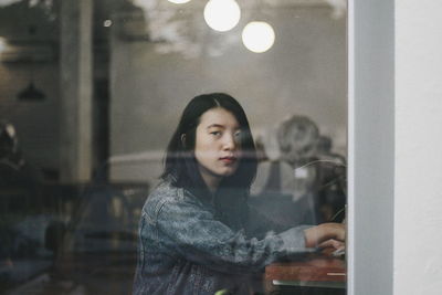 Portrait of young woman looking through glass window
