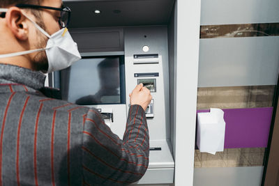 Business man with protective face mask using street atm machine.