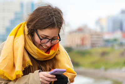 Smiling warm young woman with her cell phone in a seaside town