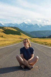 Man sitting on road against mountain range