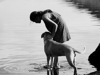 Woman stroking dog while standing at lake