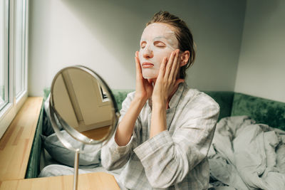 Young woman makes a beauty cosmetic face mask at home in the bedroom.