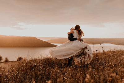 Rear view of woman standing on field against sky during sunset