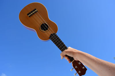 Cropped hand of woman holding ukulele against blue sky