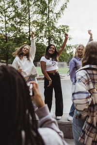 Smiling female friends with hand raised dancing on retaining wall at skateboard park