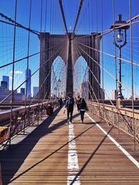 People walking on brooklyn bridge against blue sky