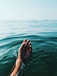 Cropped hand of woman in sea against sky