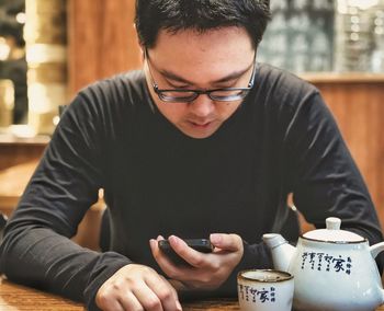 Young man using mobile phone while drinking chinese tea.