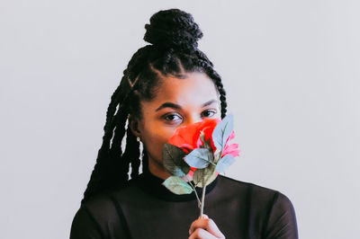 Portrait of young woman holding flowers against white background