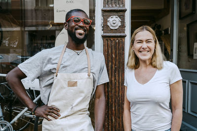 Portrait of cheerful owners standing against bicycle shop