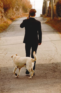 Rear view of man walking with dog on footpath