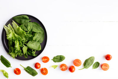 Bowl of fresh salad leaves, lettuce, spinach and red cherry tomatoes and halves on white background