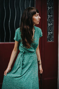 Young woman looking away while standing against door