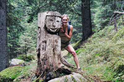 Portrait of woman standing by tree trunk in forest