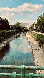 Footpath by canal in city against sky