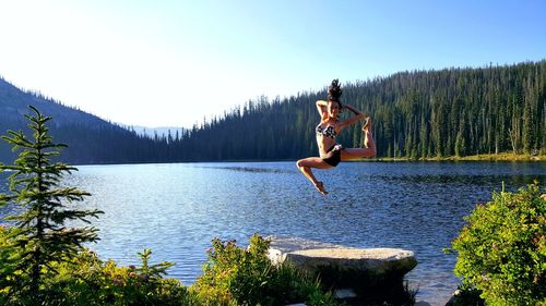 Woman jumping on lake against trees in forest