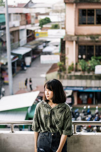 Young woman standing in balcony against buildings in city