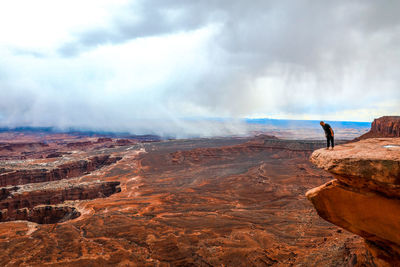 Man looking over canyonlands at the edge of a large rock