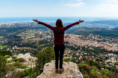 Rear view of woman with arms outstretched standing on cliff against sky