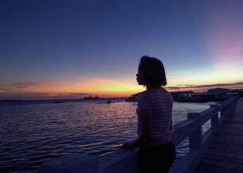 Rear view of woman looking at sea against sky during sunset