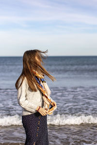 Rear view of woman standing at beach against sky