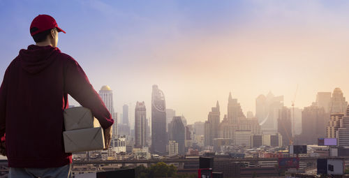 Rear view of man looking at city buildings against sky