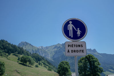 Road sign by mountains against clear blue sky