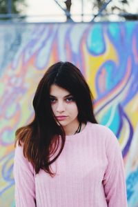 Portrait of beautiful young woman standing against graffiti