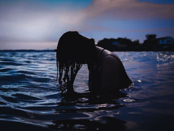 Silhouette woman in sea against sky during sunset