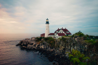 Lighthouse amidst sea and buildings against sky