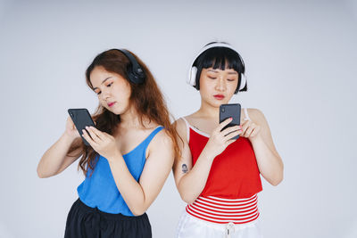 Lesbian couple using phone while listening music against gray background