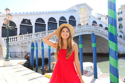 Young woman wearing hat looking away against bridge over canal