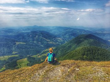 Rear view of woman sitting on mountain against cloudy sky