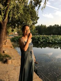 Portrait of woman standing on footpath by lake