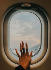 Cropped image of hand against sky seen through airplane window
