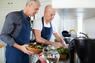 Mature men talking while cooking food in kitchen at home