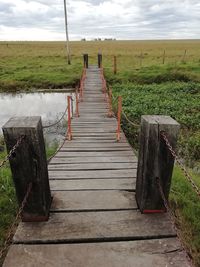 Wooden boardwalk on field against sky