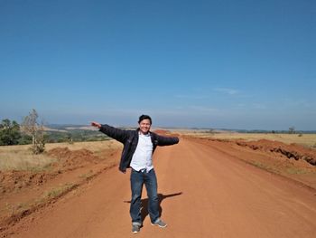 Portrait of young man standing on road against blue sky