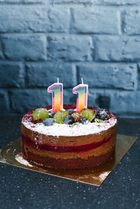 A festive fruit cake with candles with numbers 11 on a blue table.