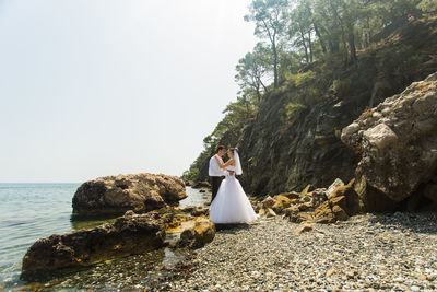 Woman standing on rock by sea against sky