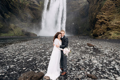 Couple standing on rock against waterfall