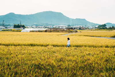 Side view of woman walking on field against sky