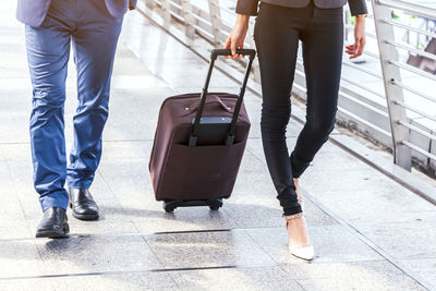 Low section of woman with luggage by man walking on elevated walkway