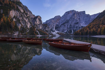 Boats moored in lake by mountains against sky