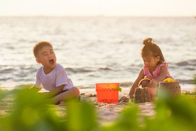 Cute sibling playing on beach against sky