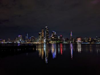 Illuminated buildings by river against sky at night