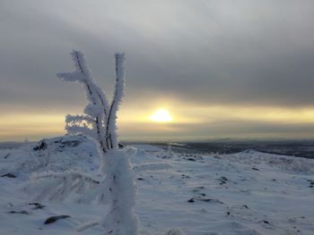 Snow covered land against sky during sunset